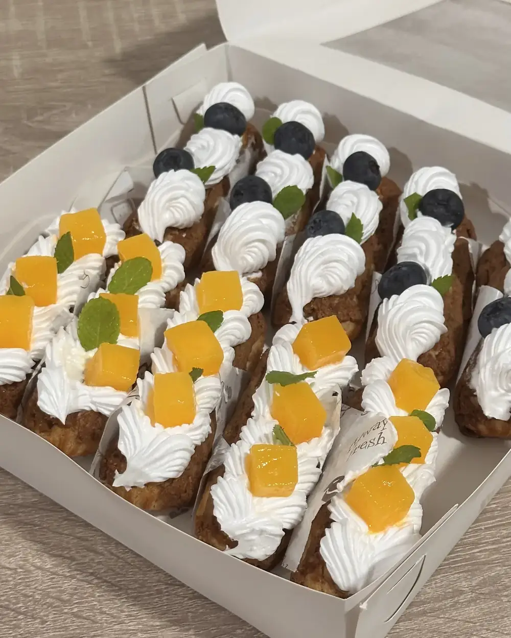 Box berisi 10 éclair dengan topping mangga dan blueberry